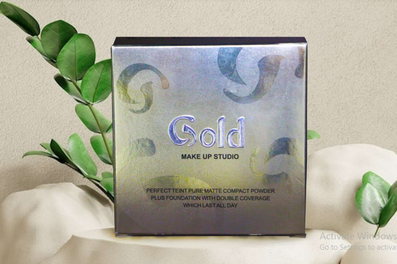 A square metallic compact powder box for Gold Make Up Studio, featuring a holographic silver and blue finish with gold swirl patterns, set against a neutral gray background.