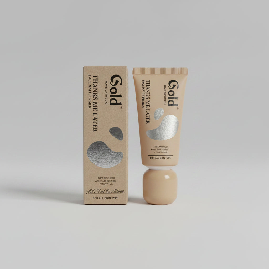 A tube of Gold Skin Makeover Thanks Me Later Face Mottles next to its matching cardboard packaging box, both in a warm beige shade with a metallic silver abstract shape, set against a neutral gray background.